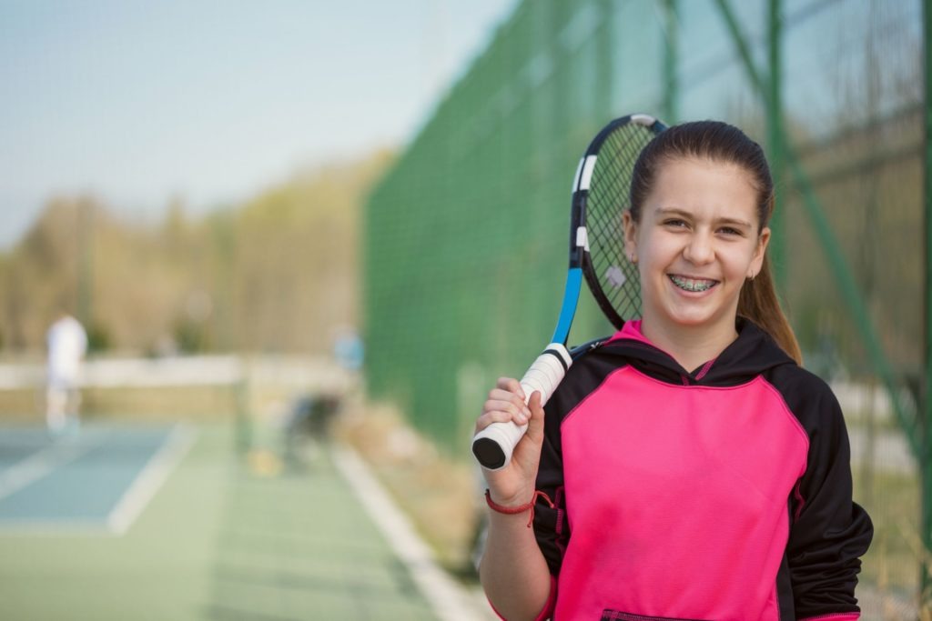 Smiling Young Girl With Braces Posing Holding A Tennis Racket